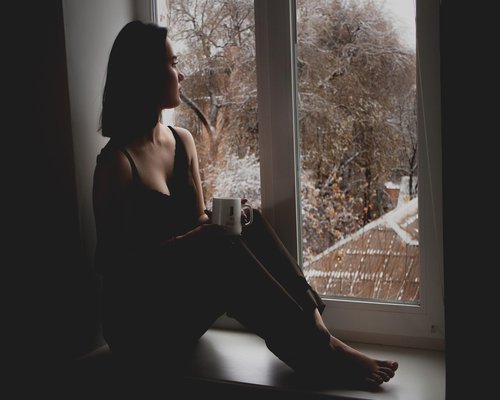 A person looking out the window in the morning holding a mug